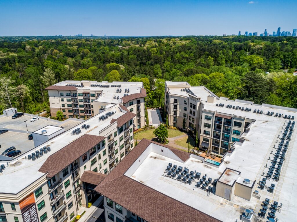 Sky view of apartment community with view of courtyard, pool, and parking. Trees in the background with atlanta skyline in the distance.