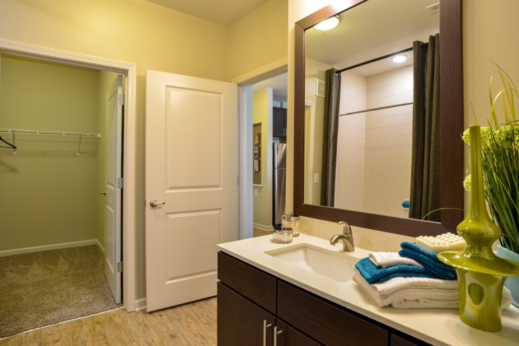 Bathroom with wood floor, marble countertop, large mirror, and view of walk in closet