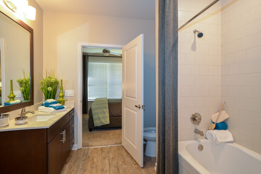 Bathroom with bathtub, wood floors, marble counter, large mirror and view of bedroom.