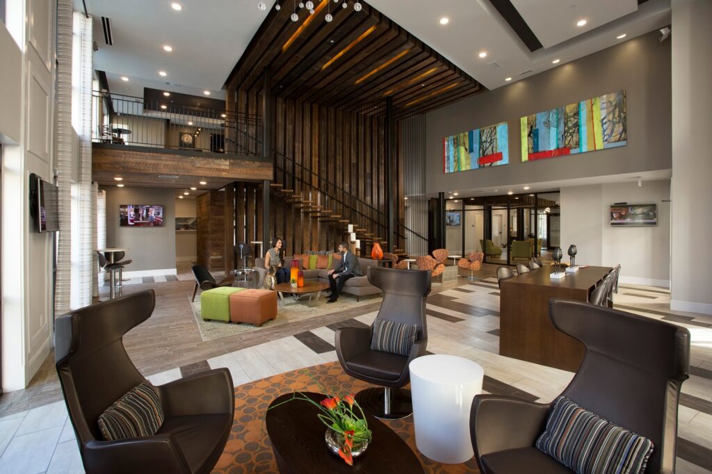 Clubhouse seating areas with a man and woman sitting on couch and chairs and table with barstools. With stairs leading up to the game area.