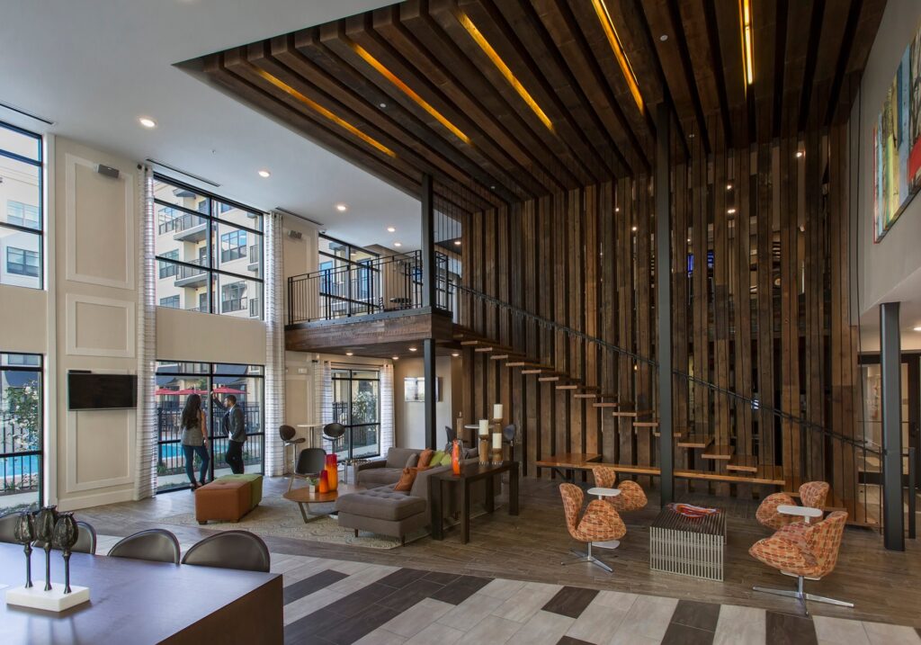 View of clubhouse sitting area with couches and chairs. Wooden accent wall with stairs leading up to kitchen and game area.