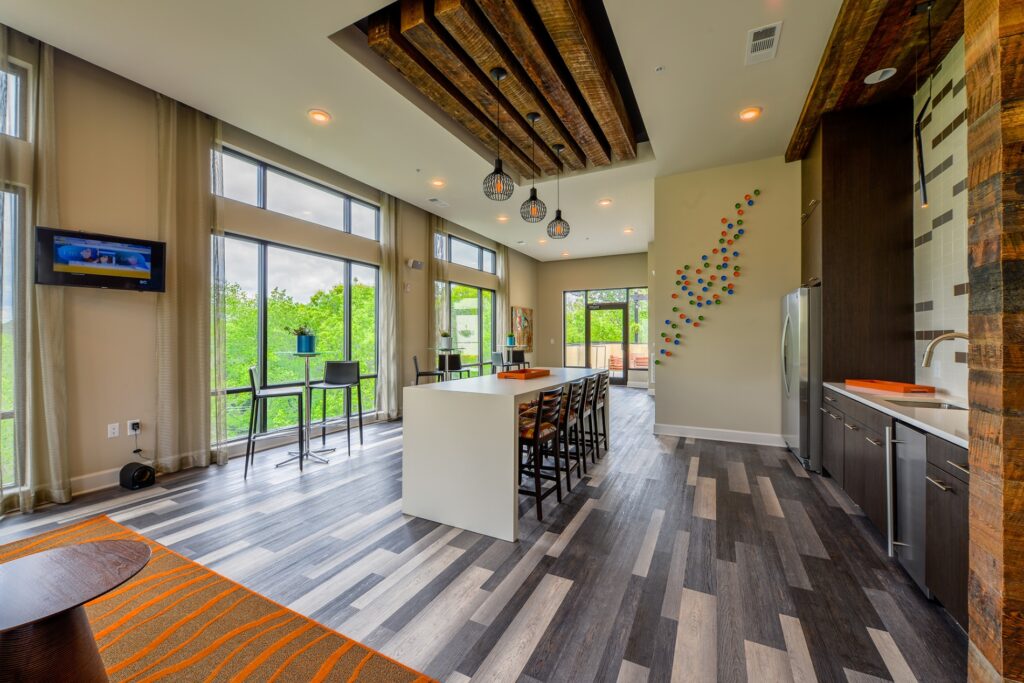 Kitchen area of club house with tables and stools. Fridge and ink. and tv mounted on the wall.