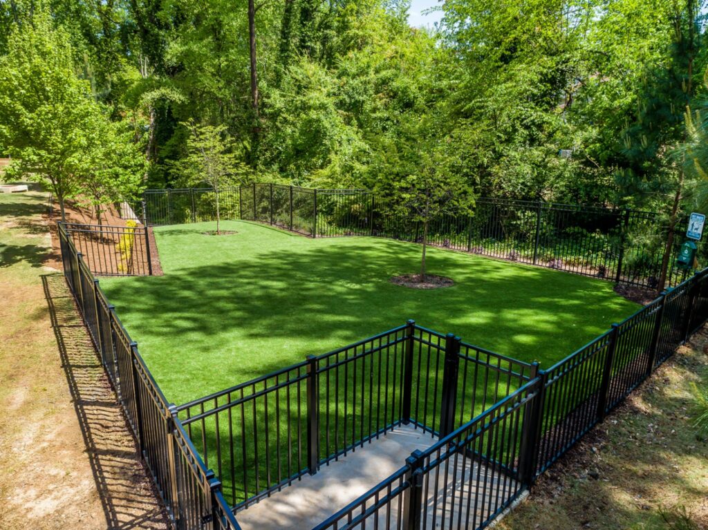 Gated dog park with trees and trash area for dog waste.