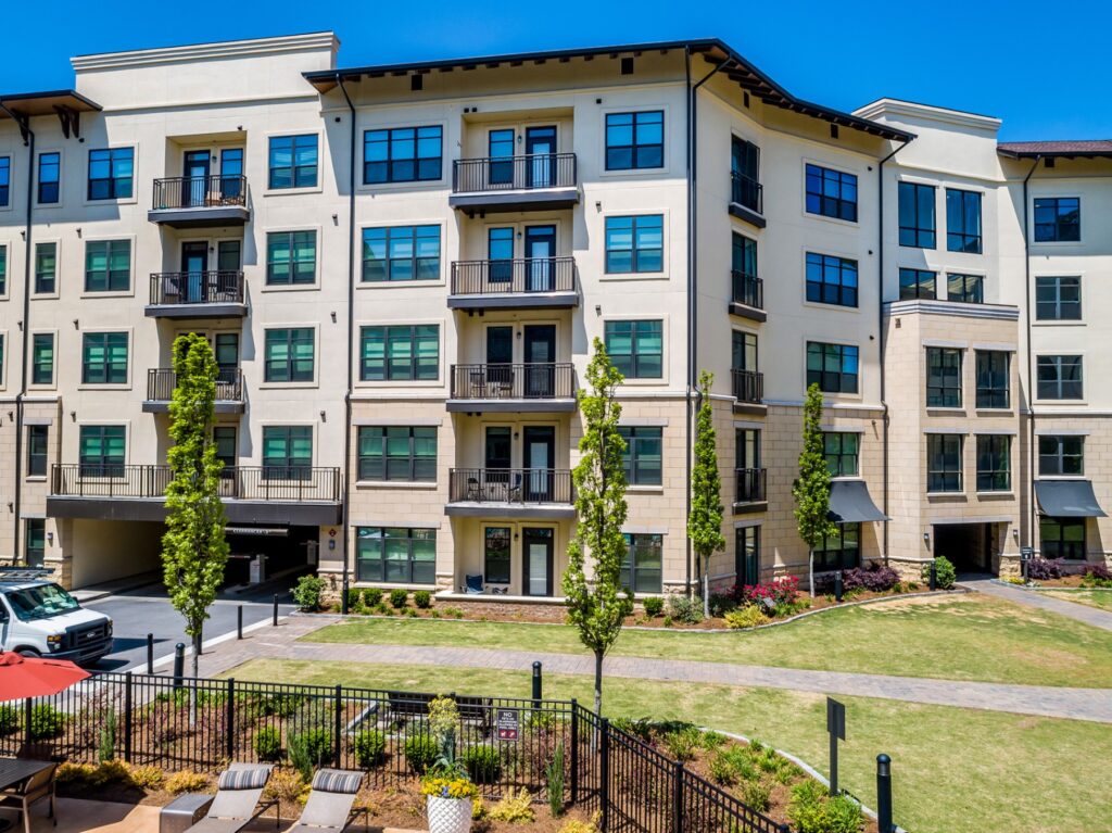 View of residential building with walkways leading to courtyard. Lots of grass and scattered trees.