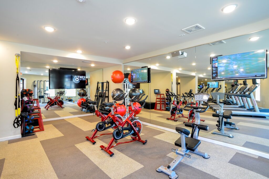 Fitness center with cardio and strength equipment. TVs mounted on walls.