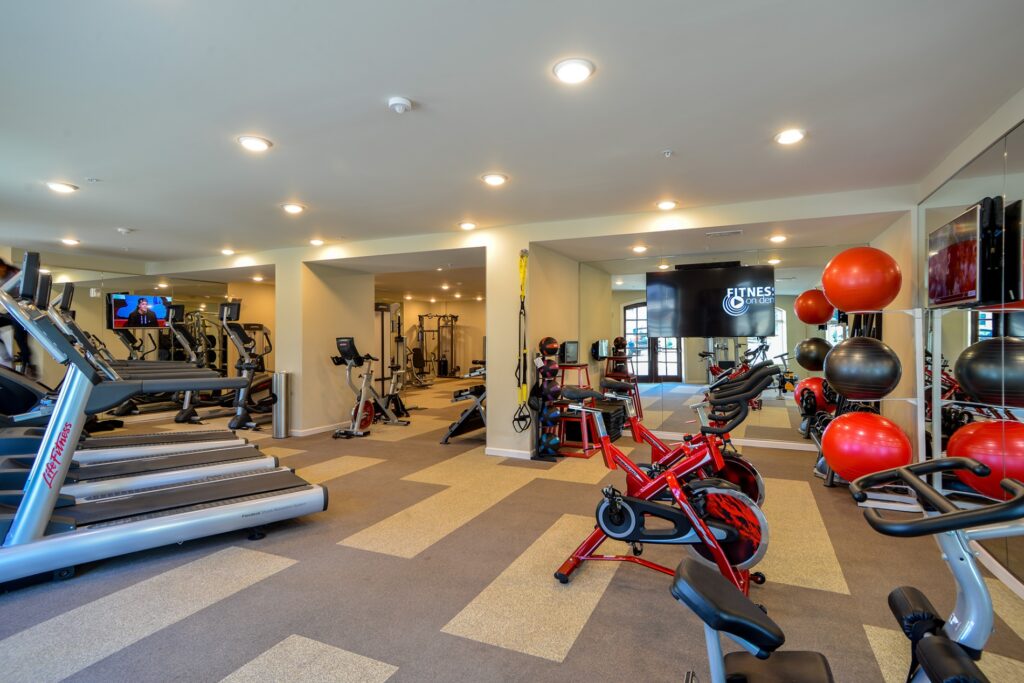 Fitness center with cardio and strength equipment. TVs mounted on walls.