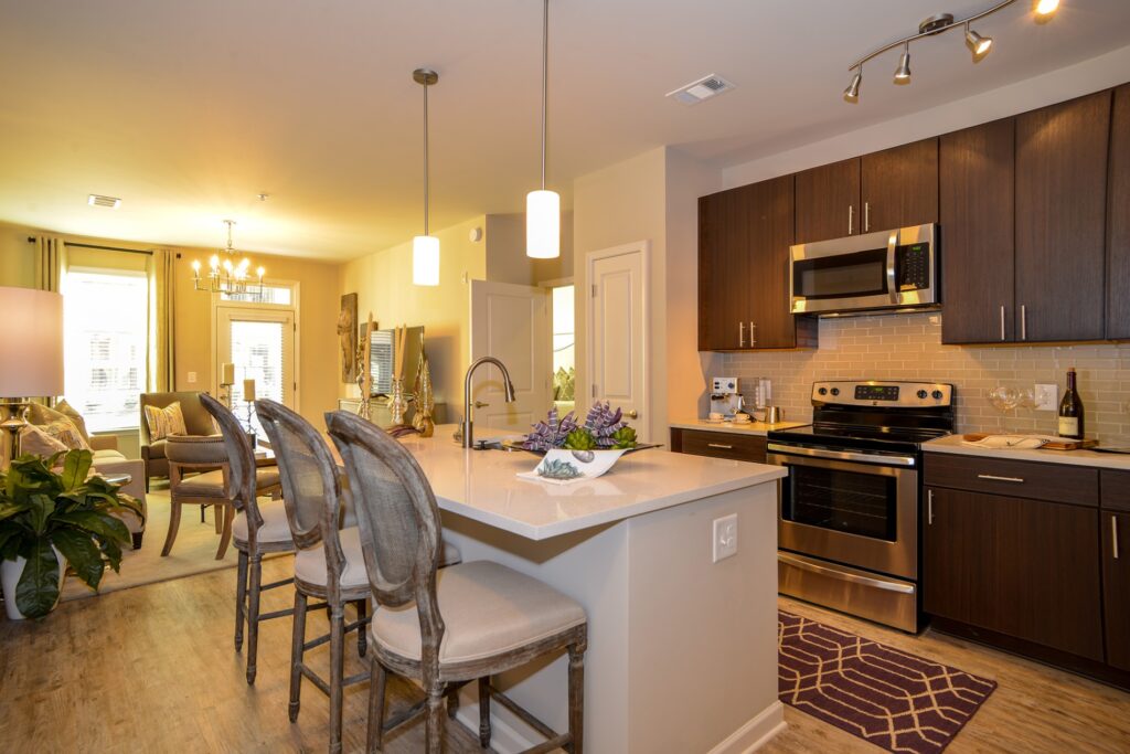 Kitchen island with granite counter top with bar stools, stainless steel appliances, and view of living area.