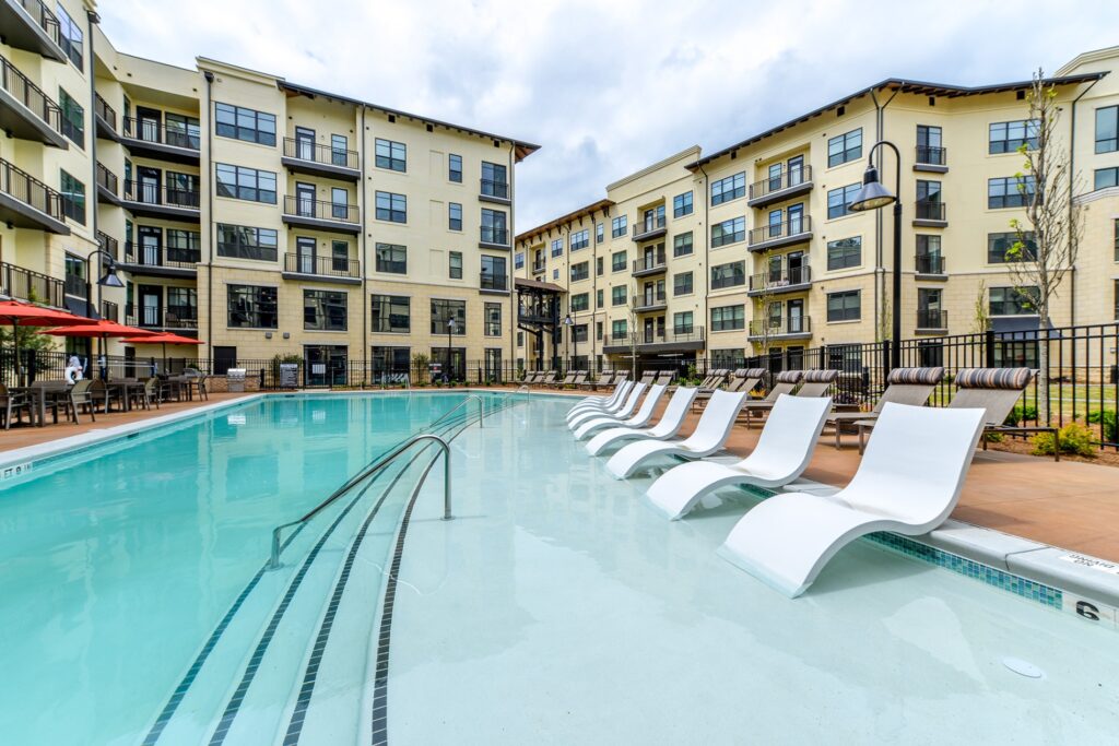 in pool seating with pool view. Lounge chairs on the right of the outside of the pool and tables with umbrellas and chairs on the left.