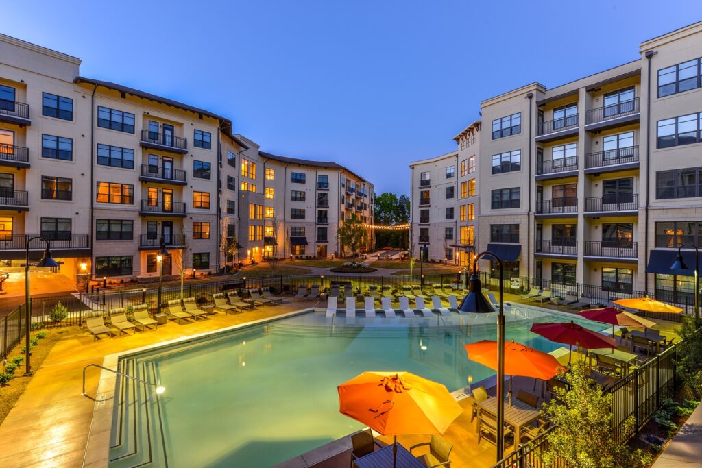 Evening view of in pool seating with pool view. Lounge chairs on the right, left and behind the outside of the pool and tables with umbrellas and chairs on the far right.