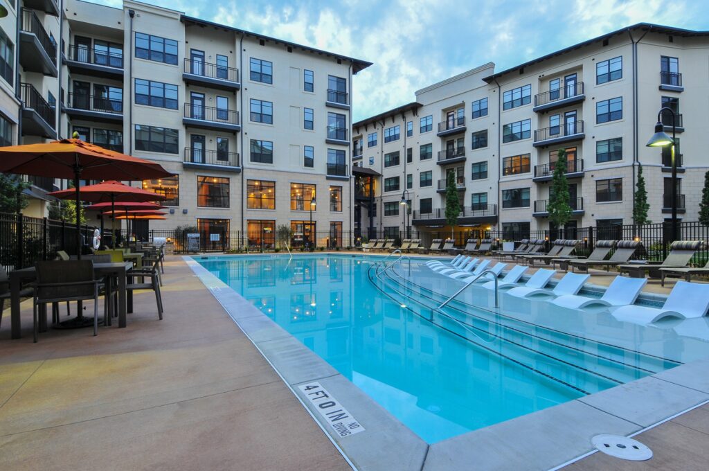 in pool seating with pool view. Lounge chairs on the right of the outside of the pool and tables with umbrellas and chairs on the left.